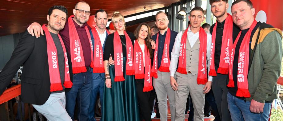 Gruppe von Personen, die alle einen roten Schal tragen, auf dem "Meister 2026" steht