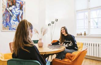 2 Frauen an einem Tisch, die miteinander sprechen