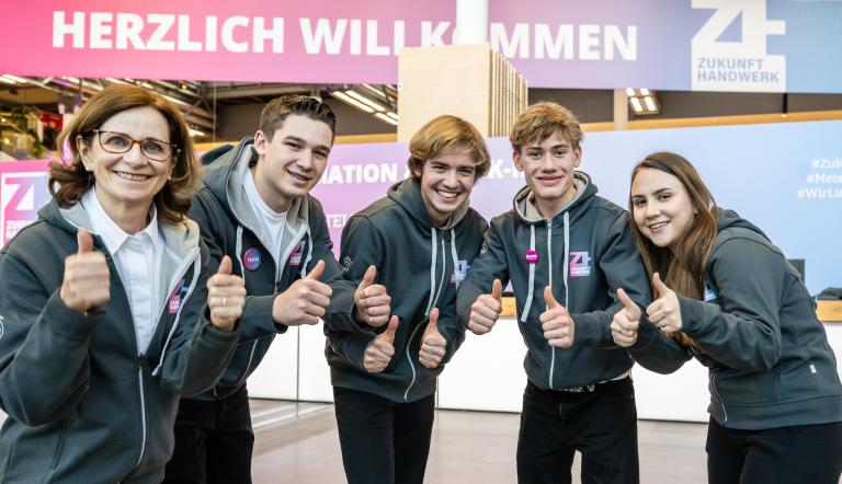5 Personen auf dem Kongress Zukunft Handwerk lächeln in die Kamera mit hochgehaltenen Daumen