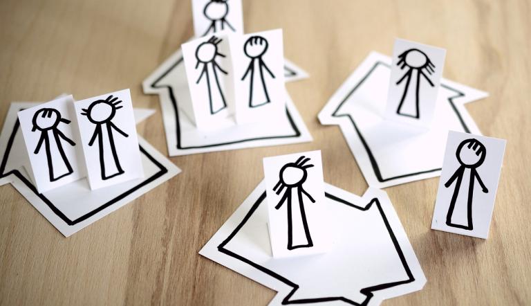 Menschenfiguren aus Papier, die in 4 Papierhäusern verteilt sind